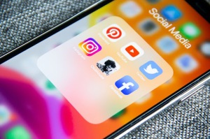 A smart phone screen is one with a group of social media icons open. Pinterest, YouTube, Twitter, Instagram, Clubhouse, and Facebook icons are all present.